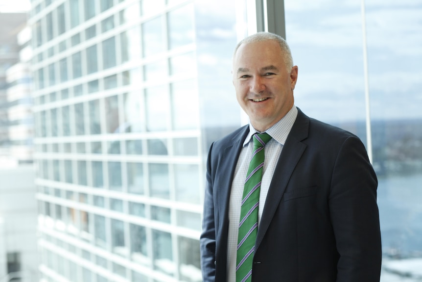 Tim Lawless smiles while wearing a suit pictured in front of glass windows