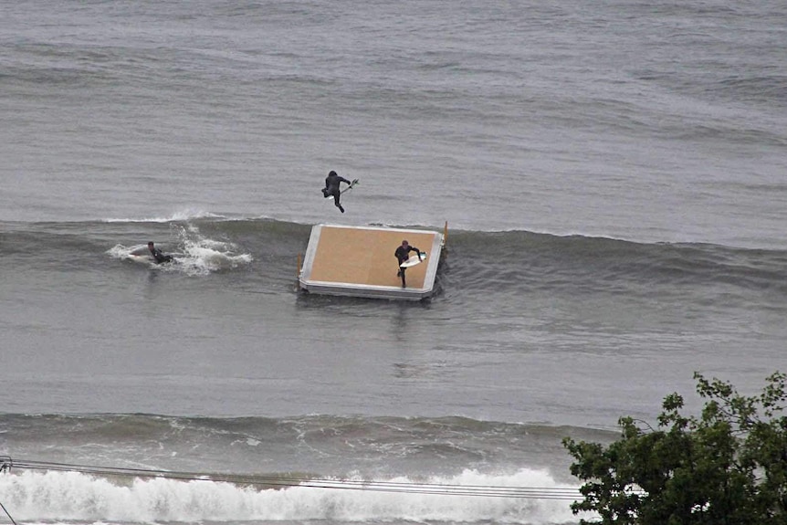 Surfers dive into the water off a pontoon