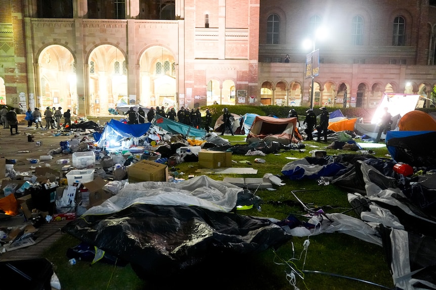 Rubbish and tents are strewn across a lawn in front of a red-brick building