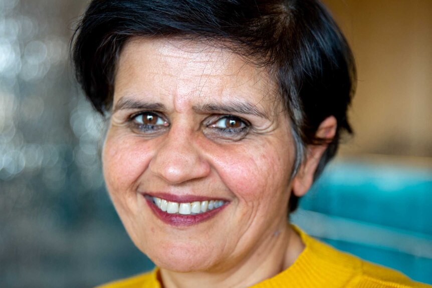 portrait of South Asian woman smiling with cropped black hair wearing yellow sweater