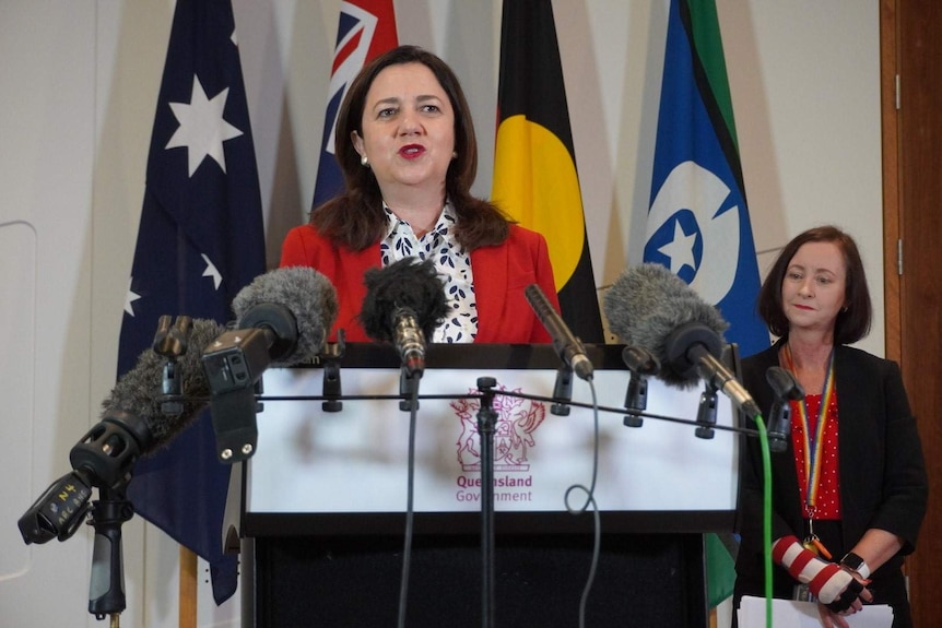 A woman speaks in front of microphones.