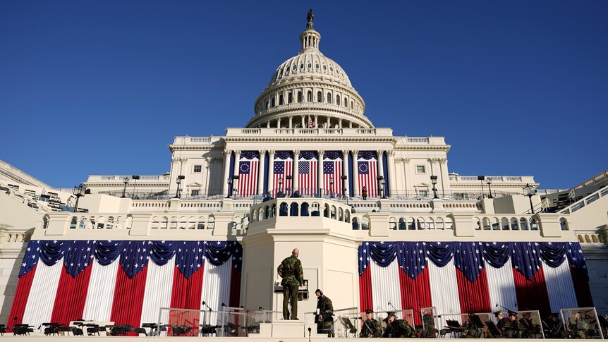 People attend to decorations and seating in front of the US Capitol, clad in American flags