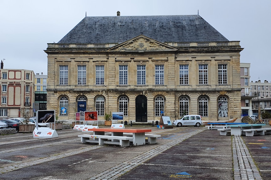 Two story historic building in France with bench and table out front and signs 