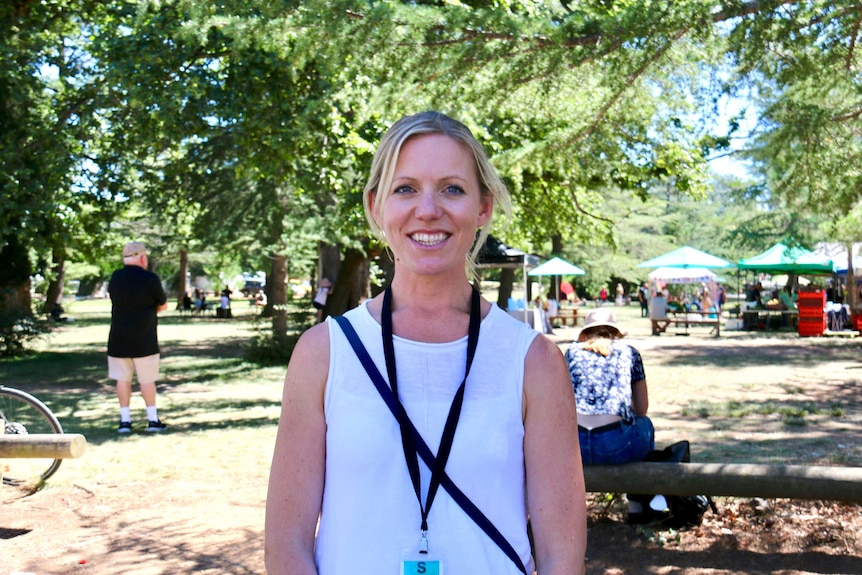 A woman smiles at the camera, with market stalls visible in the background.