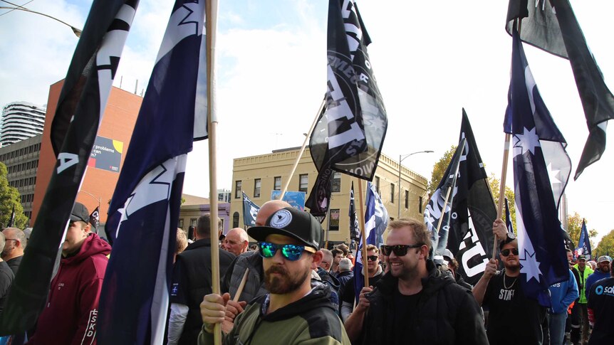 CFMEU flags are waved by union protesters as they march down Russell Street demanding an increase to the minimum wage.