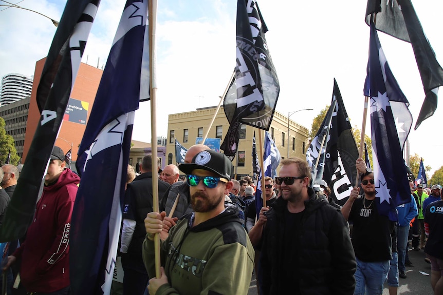 CFMEU flags are waved by union protesters as they march down Russell Street demanding an increase to the minimum wage.