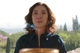 Michelle Yeoh holds a tray with burning incense in it, appearing to provide an offering at a temple, while her eyes are teary.