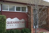 A red school with a sign reading 'Queanbeyan High School'.