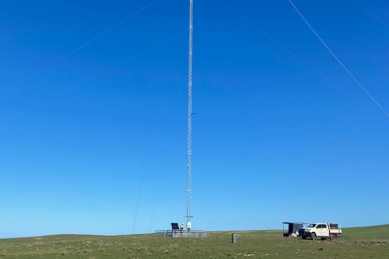Large thin tower with vehicle nearby in open paddock, clear blue sky