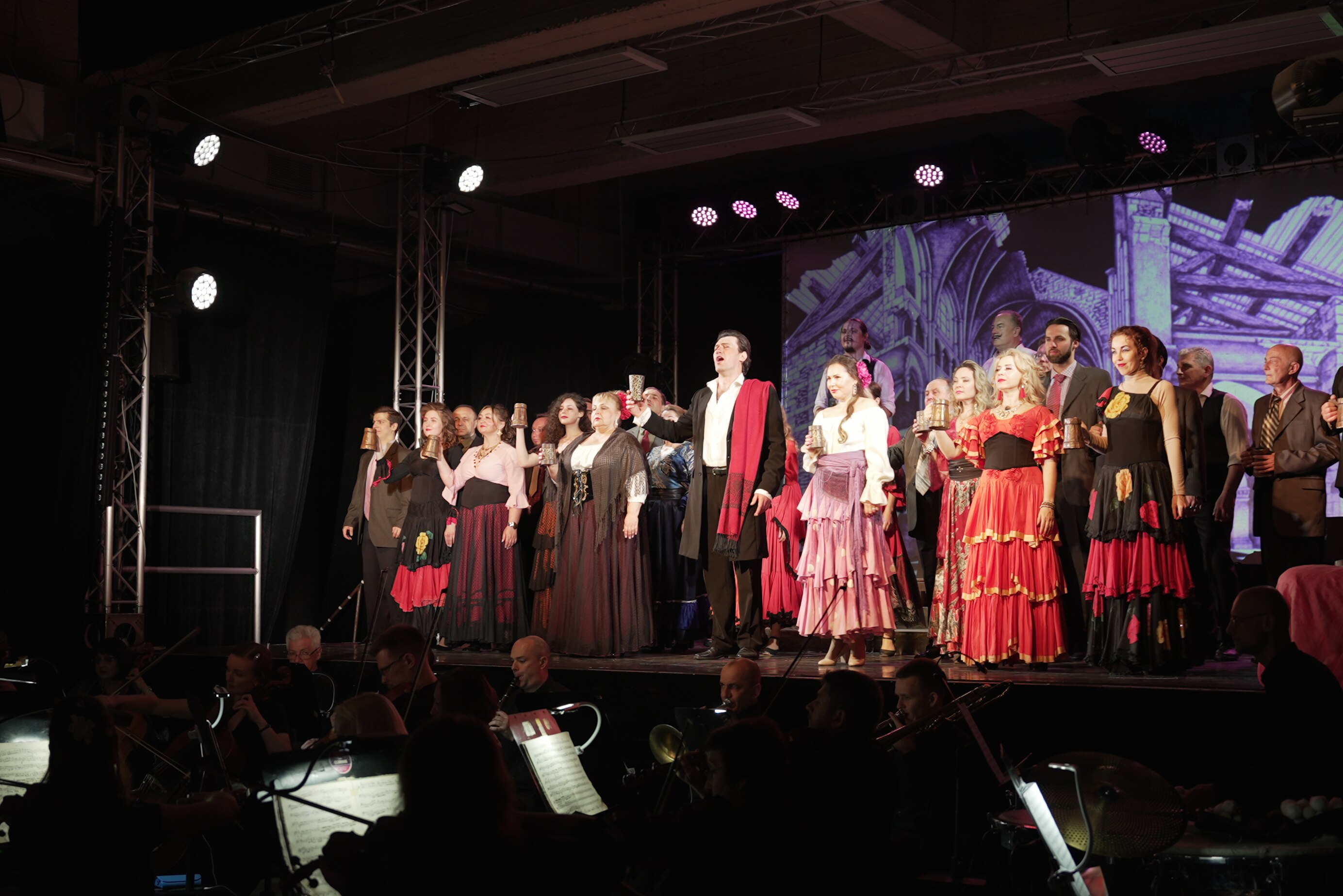 A stage full of performers and singers, below an orchestra is seated.