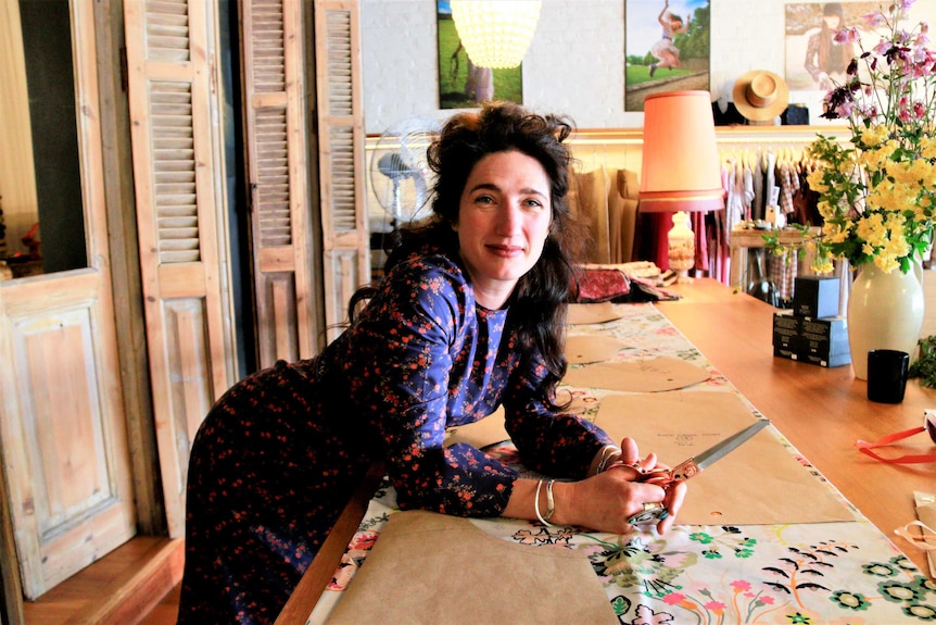 Woman in floral dress leans over desk with patterned fabric in fashion store.