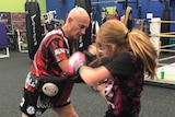 Coach Joe Hilton holds pads for young girl to use her knees in thai boxing gym