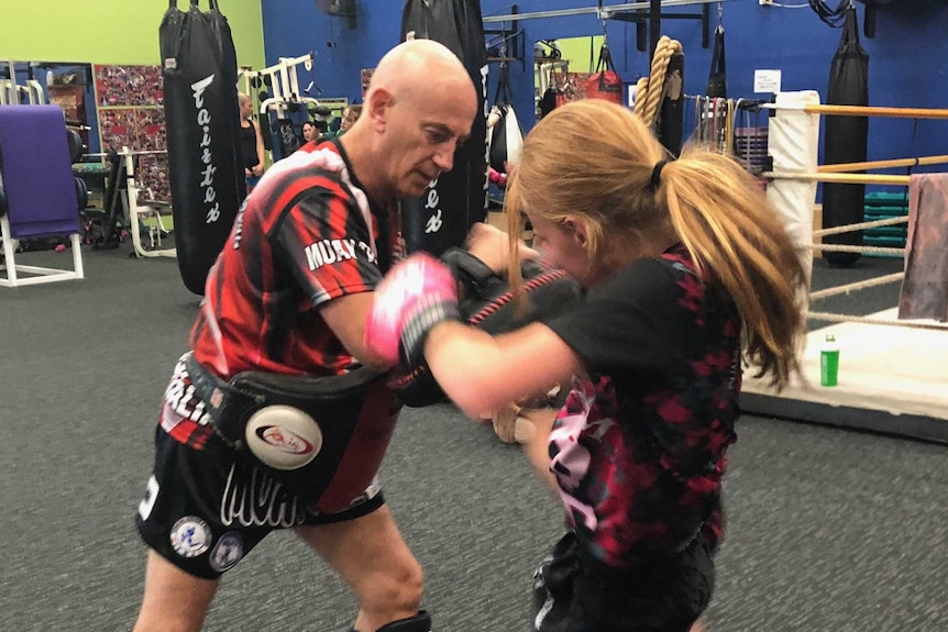 Coach Joe Hilton holds pads for young girl to use her knees in thai boxing gym
