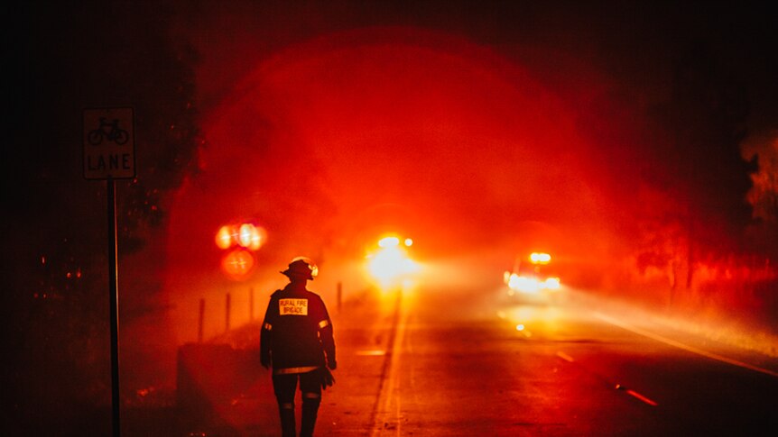 A rural firefighter walks towards headlights on a highway in south-east Queensland.