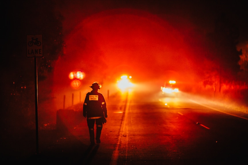 A rural firefighter walks towards headlights on a highway in south-east Queensland.