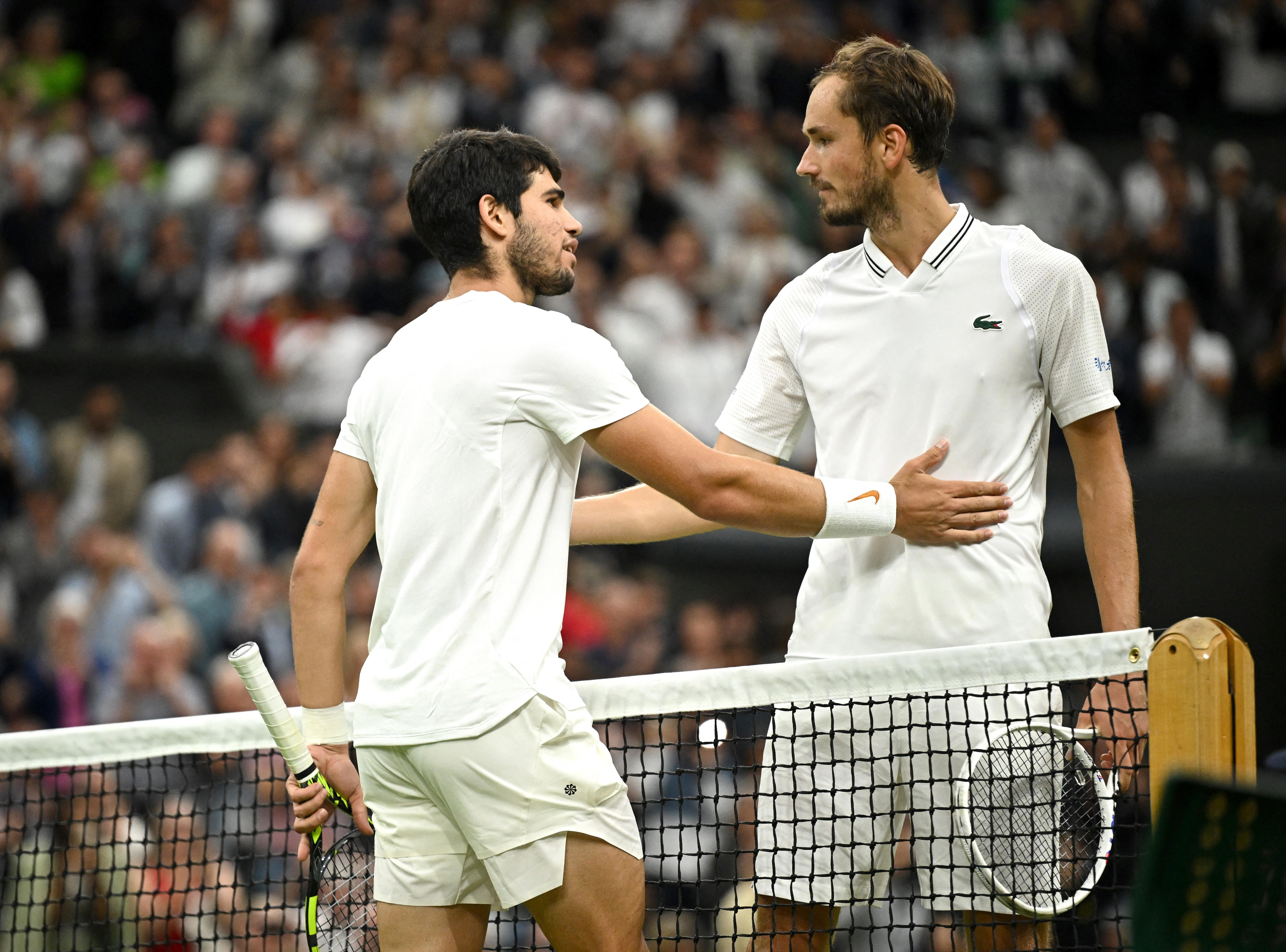 Two men wearing white clothes holding tennis rackets, arms over each other