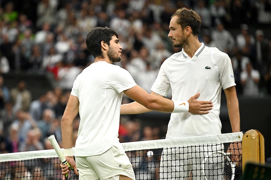 Two men wearing white clothes holding tennis rackets with their arms on each other