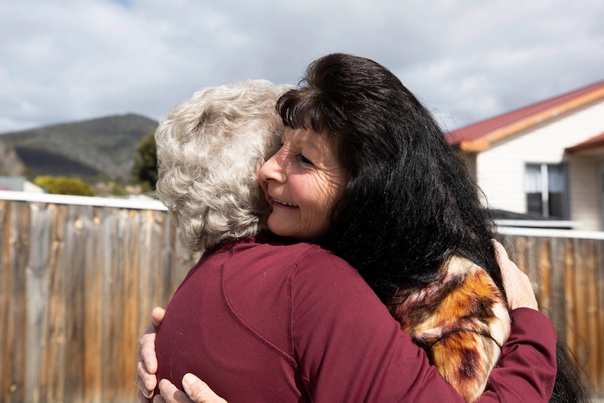 A woman with long black hair hugs an elderly woman