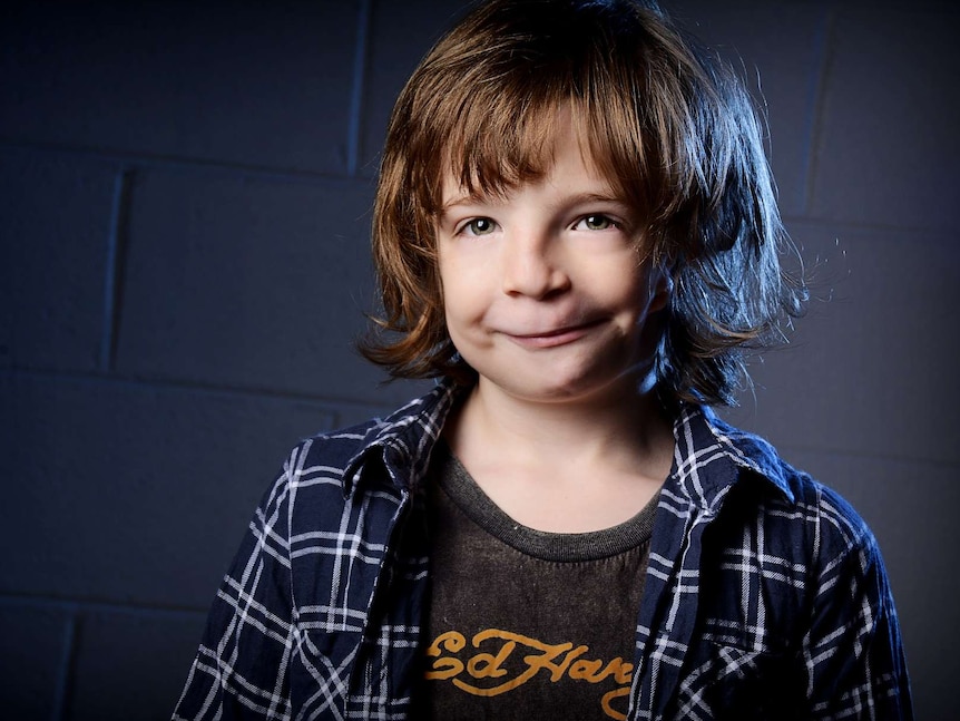 Eight year old boy with hair to chin, smiling cheeky at the camera