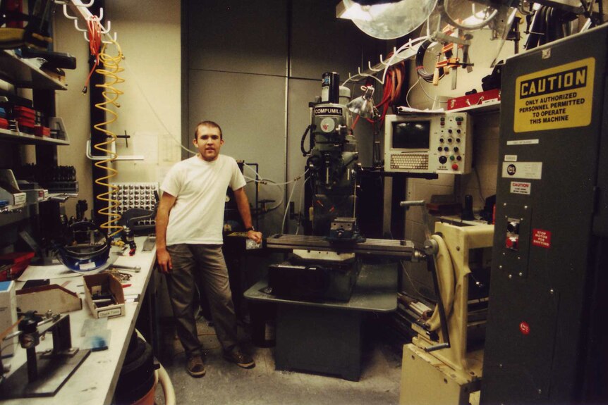 An old photo of a young man standing in a cluttered engineering laboratory.