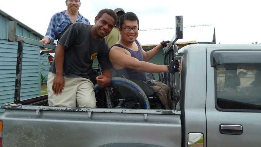 Huy is in the back of a ute in his wheelchair surrounded by three men. They are smiling.