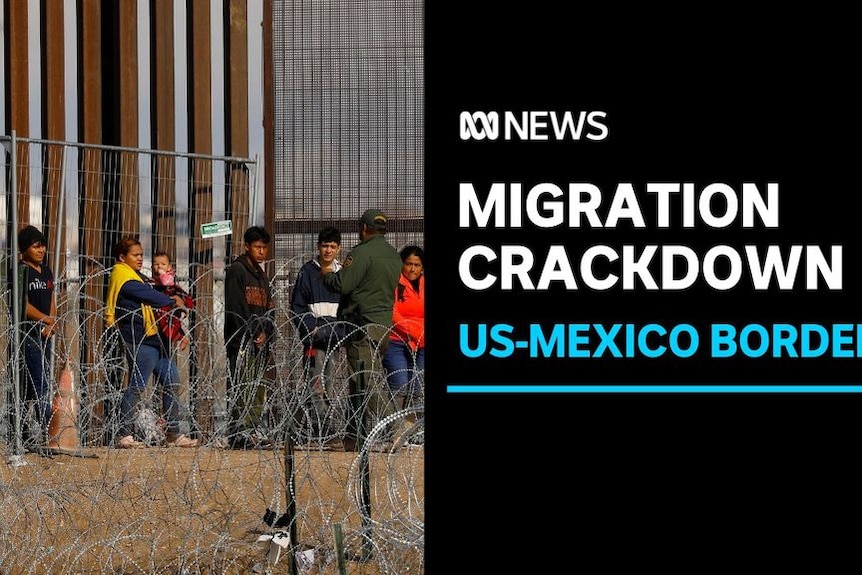 Migration Crackdown, US-Mexico Border: A row of people lined up behind razor wire next to a border wall.