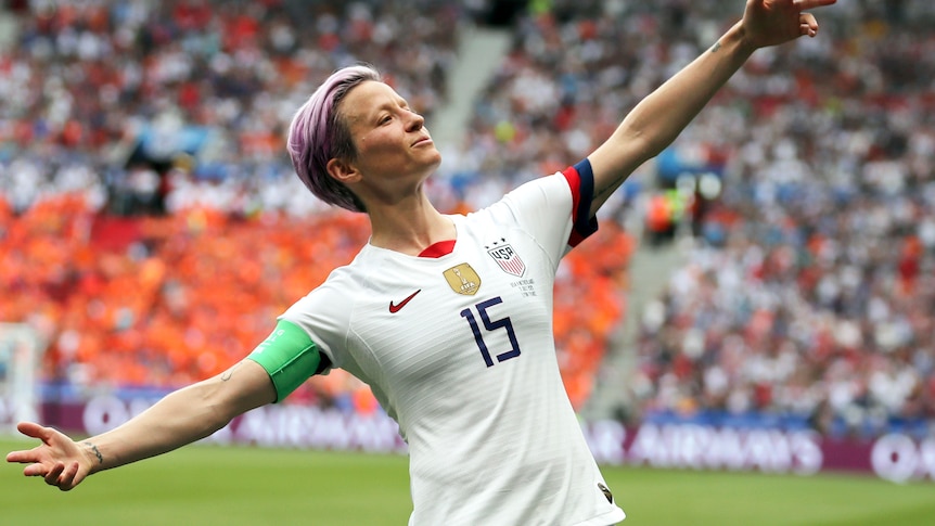 Megan Rapinoe on a soccer field, spreading her arms wide in celebration