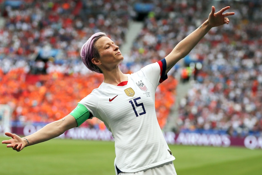 Megan Rapinoe on a soccer field, spreading her arms wide in celebration