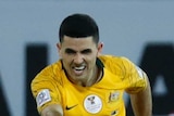 Australia player Tom Rogic strikes the ball while grimacing in the face.