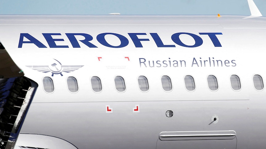 A section of a silver plane with blue writing and 10 small windows. 