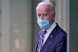 Joe Biden in a blue suit with a blue face mask walks outside