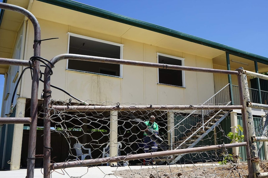 Rundown house behind a wire gate.