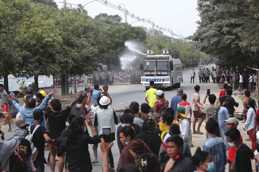 An armoured police truck uses a water cannon to disperse a crowd of protesters.