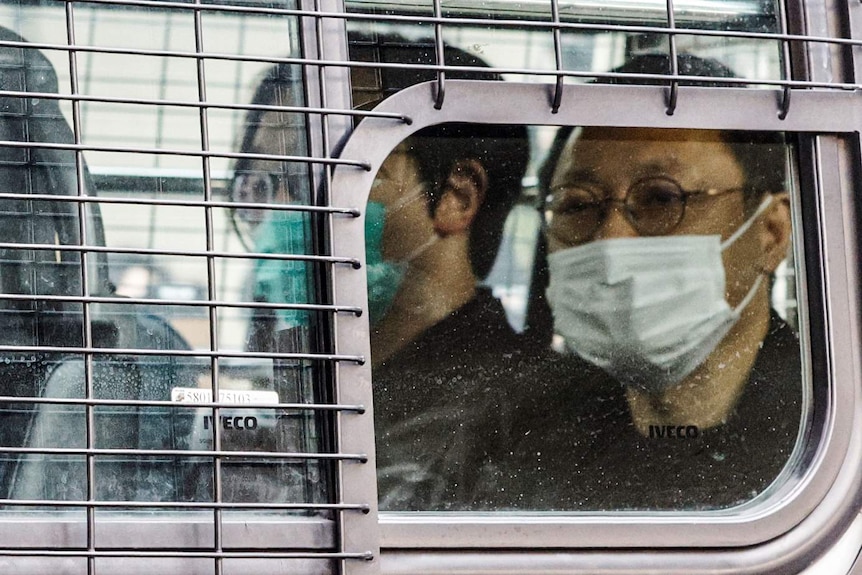 Two middle-aged Chinese men in face mask sit behind grill inside moving truck.
