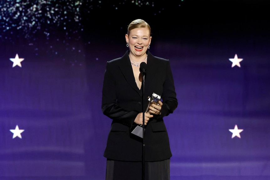 Sarah Snook smiling holding an award in front of a microphone. 