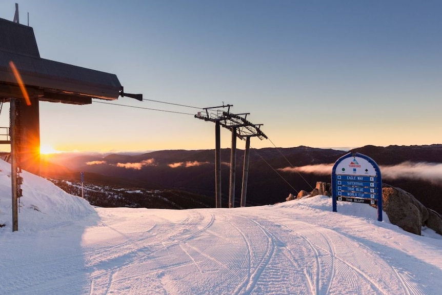 A groomed ski snow run with grooming machine, chair lift and snow making machine in the background.