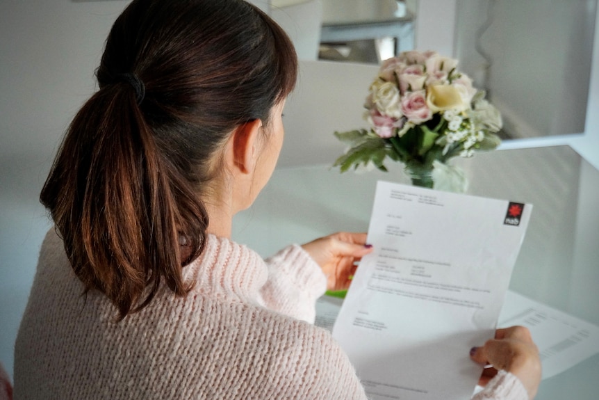 Sarah Kay is photographed from over her shoulder, as she reads a letter from NAB in her kitchen.