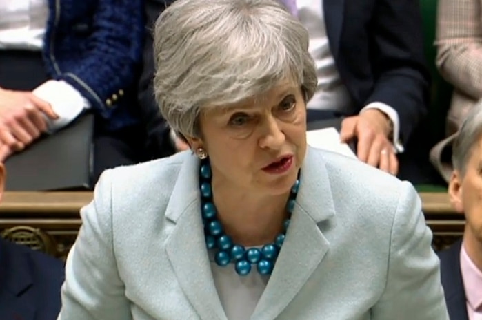 A woman stands and speaks while a group of people sit behind her.