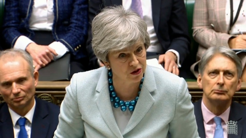 A woman stands and speaks while a group of people sit behind her.