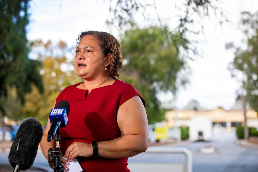 Melanie Bray wears a red business shirt as she addresses media outside a prison