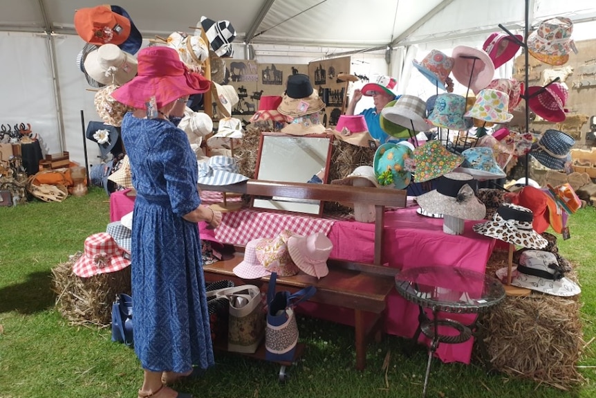 Photo of a market stall with hats and a woman standing nearby.