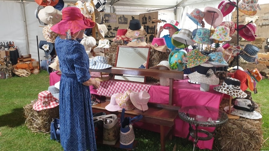 Photo of a market stall with hats and a woman standing nearby.