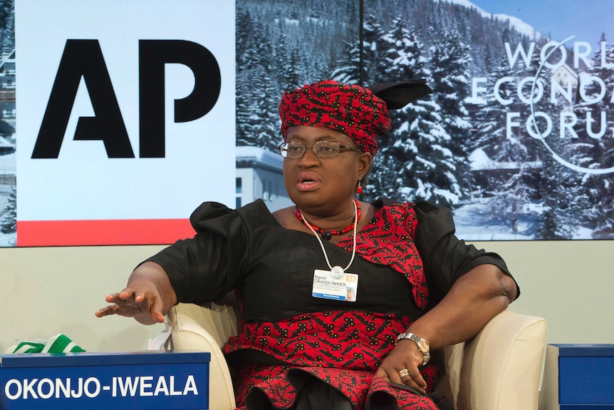 Ngozi Okonjo-Iweala sitting down during a press conference wearing a traditional dress and headwear in black and red.