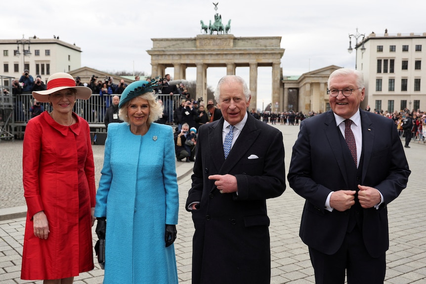From left: Elka wearing red, Camilla wearing blue, Charles and Frank-Walter in suits smile in front of the brandenburg gate