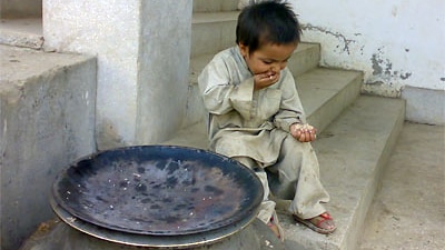 A child eats scraps of rice next to an empty rice bowl.
