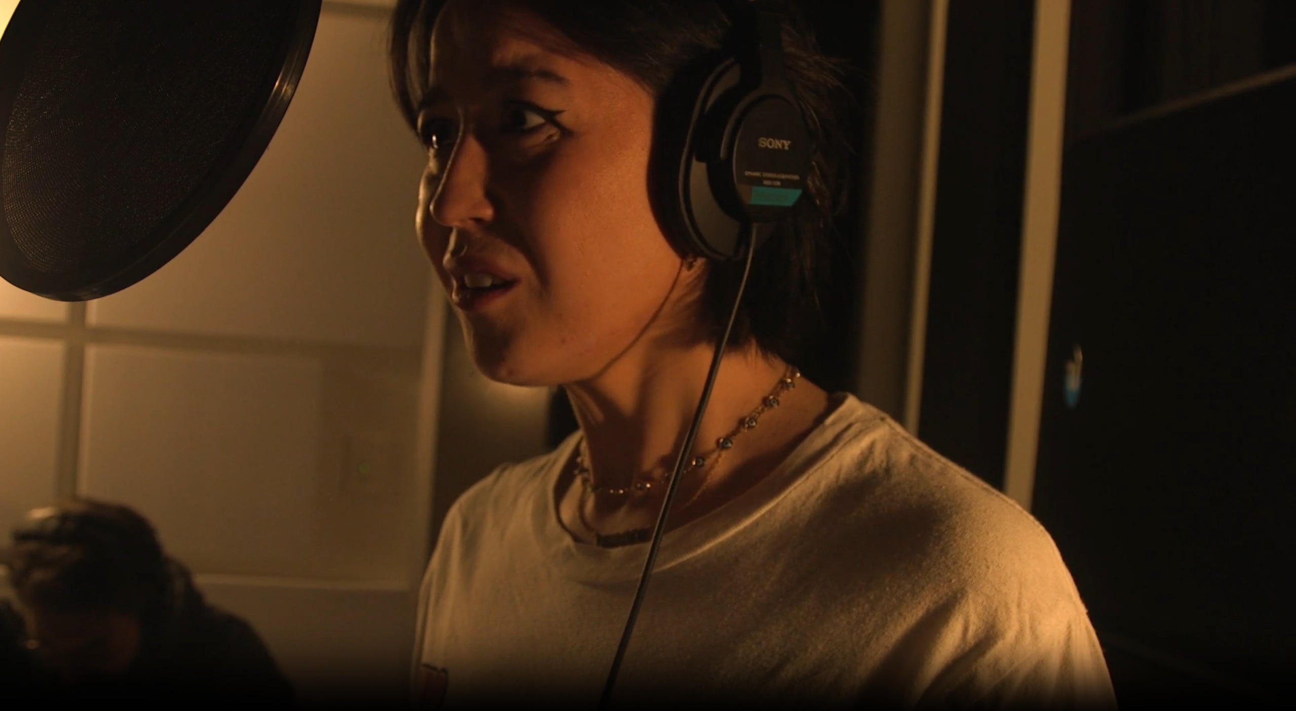 Nina Oyama habla por un micrófono con auriculares en una habitación a oscuras