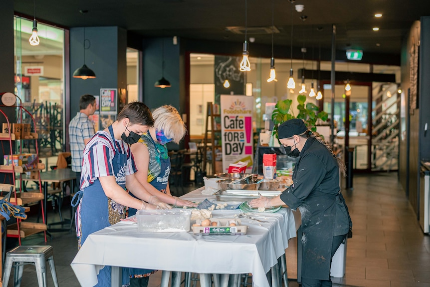 Two young people on the left hand side of table and a chef on the right hand side of table, preparing food