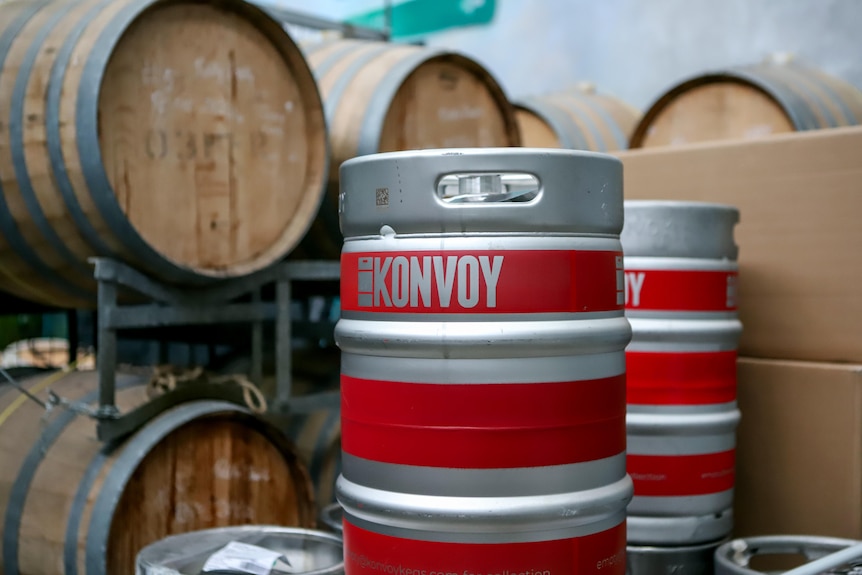 Red and silver striped beer keg sits in front of old wooden wine barrels