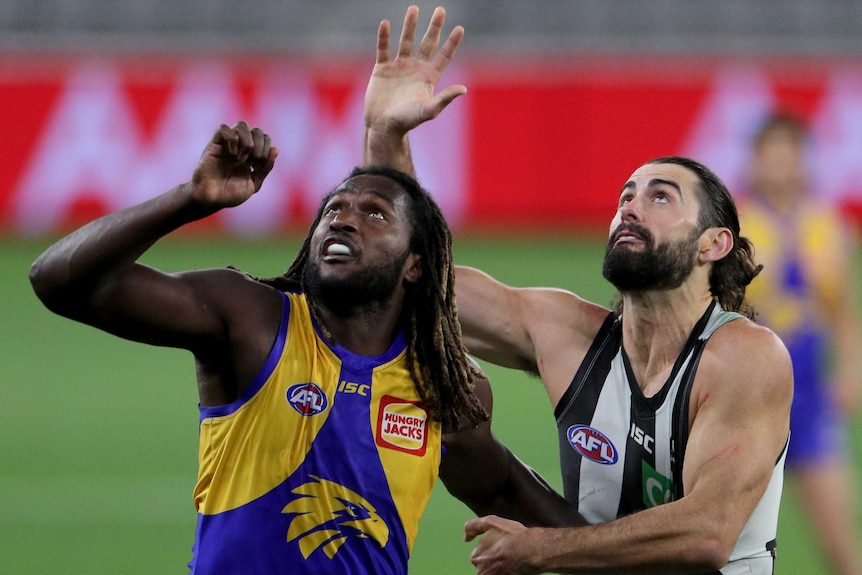 A West Coast Eagles AFL player stands next to a Collingwood opponent as they look toward the sky.