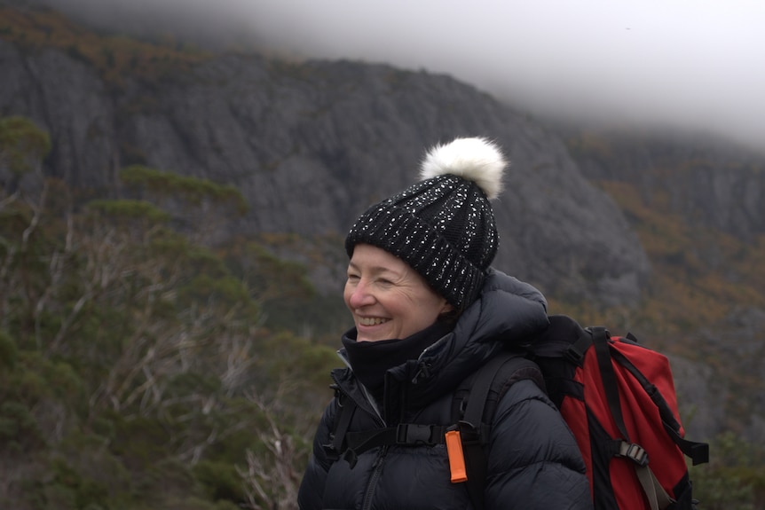 Woman wearing bobble hat wrapped up in warm coat carrying large back pack. 